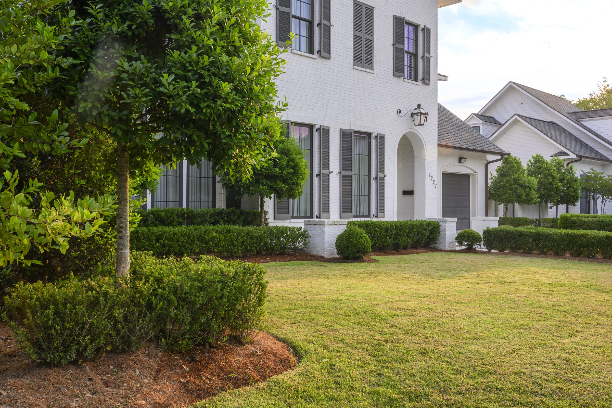 White three-story brick home with sculpted boxwood and topiary