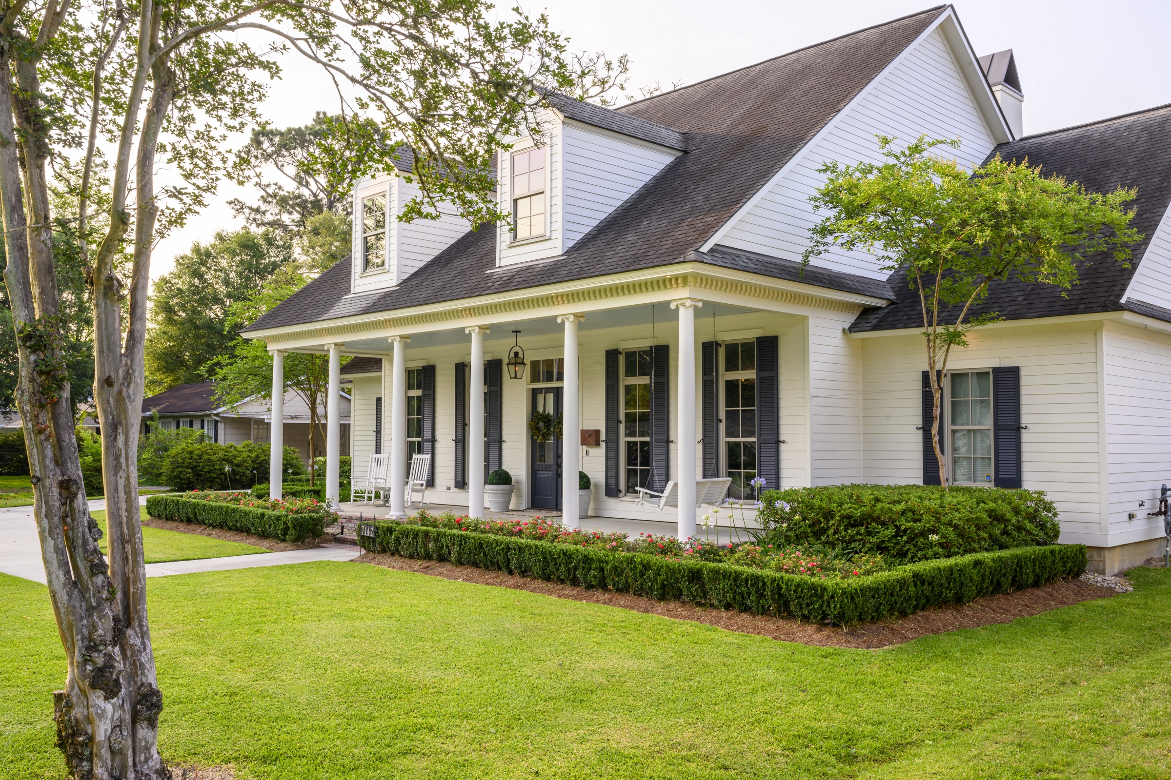 Traditional white Louisiana cottage with full porch and boxwood hedging