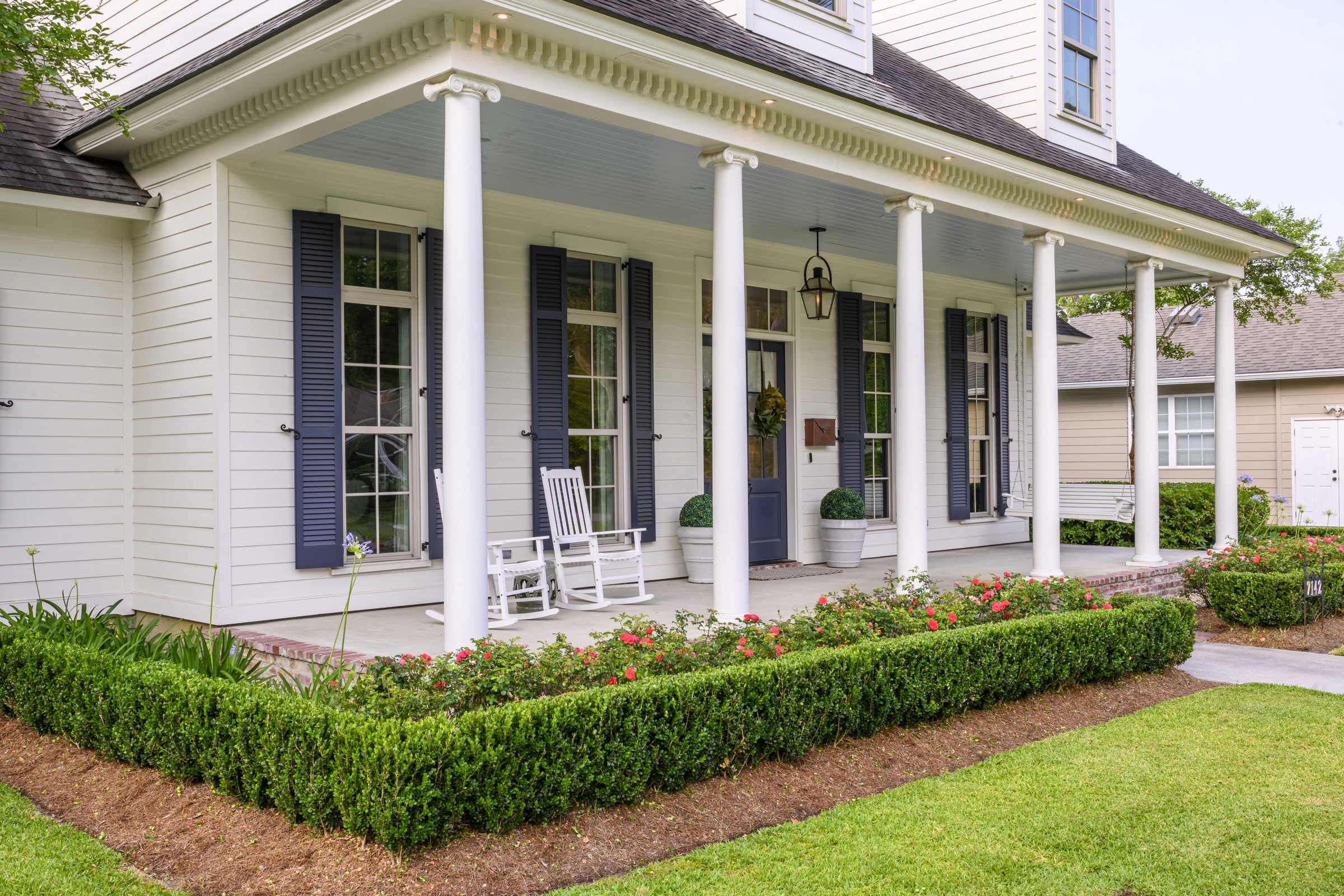 Porch detail with white columns, rockers, and boxwood frontage